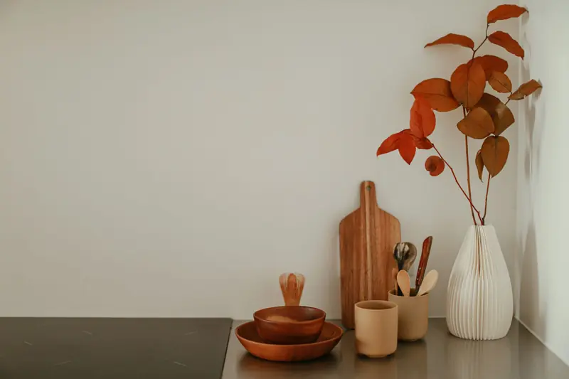 A minimalist kitchen corner with wooden bowls, a vase with autumn leaves, and cooking utensils on a countertop